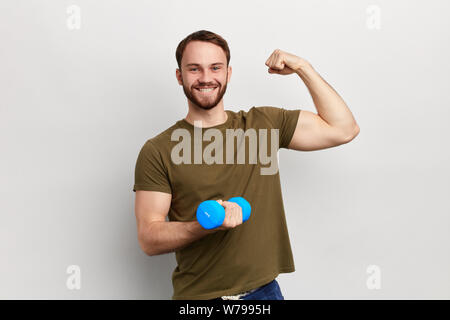 young handsome smiling man trainingwith dumbbell, showing biceps. isolated white background, studio shot, health and body care Stock Photo
