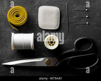 Flat lay top view sewing tools with measurement tape, chalk, thread, needles and scissors on black dark wooden table Stock Photo