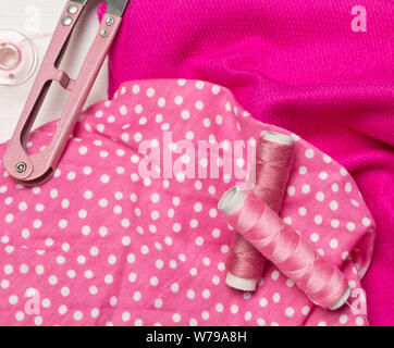 Pink colored flat lay top view sewing tools with thread and scissors on pink fabric textile background Stock Photo