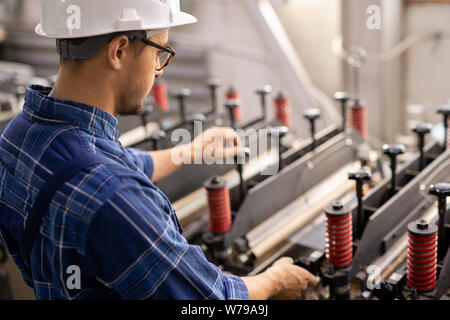 Young engineer standing by industrial machine while operating it in working area Stock Photo