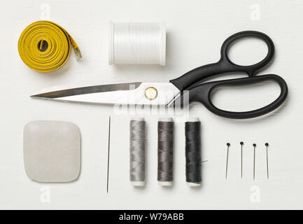 Flat lay top view sewing tools with measurement tape, chalk, thread, needles and scissors on white wooden table Stock Photo