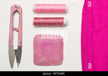 Pink colored flat lay top view sewing tools with texile fabric, chalk, thread and scissors on white wooden table Stock Photo
