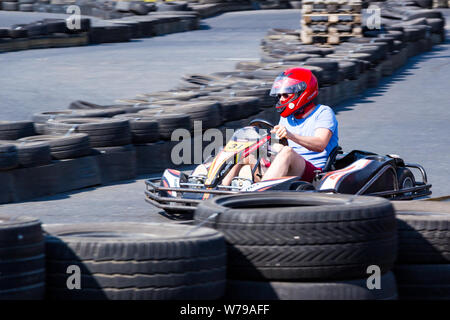 Go-kart driver in red helmet taking the bend between safety tyre barriers Stock Photo