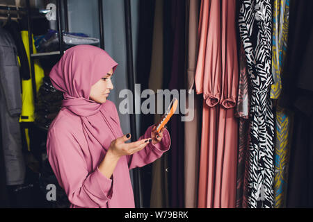 Portrait of a muslim businesswoman checks availability of goods by using the touch pad while standing in her modern shop, young female consultant Stock Photo