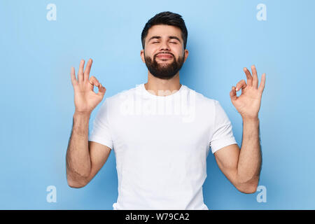 Concentrated relaxed bearded man with closed eyes doing yoga, having relaxation, meditating. harmony concept. close up portrait. isolated blue backgro Stock Photo