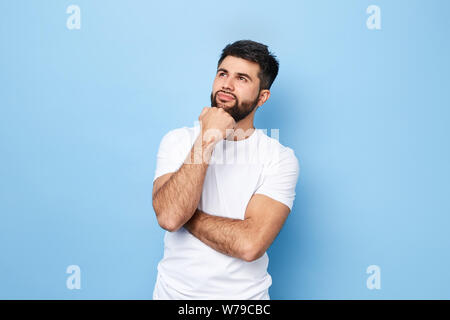 thoughtful dreaming romantic man touching his chin and weighs the pluses and minuses of the offer isolated on blue background with copy space for text Stock Photo