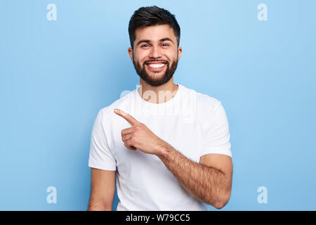 Young handsome charming man showing something with index finger, place for text, advert, copy space. isolated on blue background. direction. body lang Stock Photo