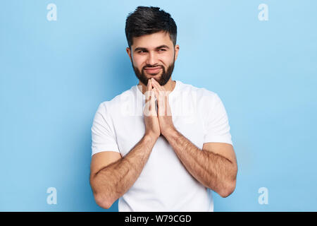 Cunning tricky thoughtful young man looking aside with palms under chin over blue background.closeup portrait, cruel plan. cruelty, negative emotion a Stock Photo