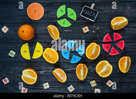 Сolorful math fractions and oranges as a sample on dark wooden background or table. Interesting creative funny math for kids. Education, back to schoo