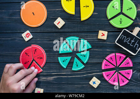 Kids hand moves colorful math fractions on dark wooden background or table. Interesting creative funny math for kids. Education, back to school concep Stock Photo