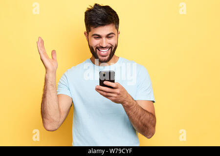 cheerful positive overjoyed man holds smart phone, reads something funny, raises palm,People and technology concept. close up portrait, isolated yello Stock Photo