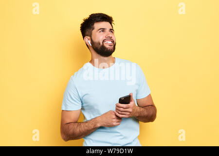 Excited cheerful man using smartphone, looking up, enjoying listening to music, isolated yellow background, studio shot. hobby, lifestyle, free time, Stock Photo