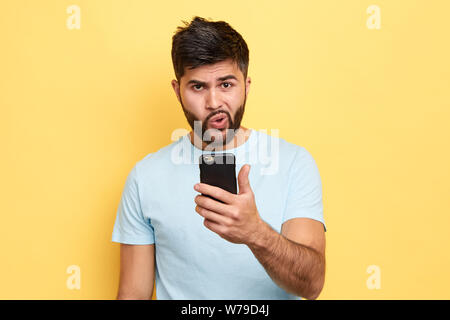 puzzled guy using his mobile phone. close up portrait. young bearded man has problems with gadget, trying to solve it. broken phone Stock Photo