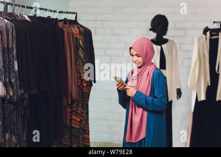 Portrait of a muslim businesswoman checks availability of goods by using the touch pad while standing in her modern shop, young female consultant Stock Photo