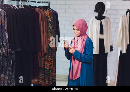 Portrait of a muslim businesswoman checks availability of goods by using the touch pad while standing in her modern shop, young female consultant Stock Photo