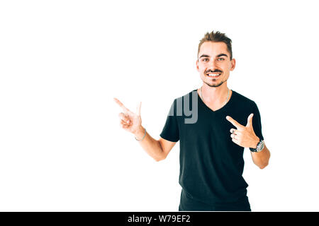 Look over here. Happy young guy in black t-shirt pointing away on white isolated background. Stock Photo