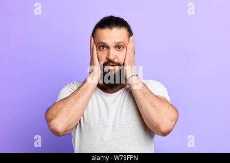 streeful terrified bearded man keeping mouth wide open, put hands on cheeks. close up portrait. isolted blue background. emotion and feeling . Oh, my Stock Photo