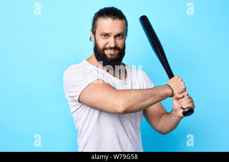 strong muscular young man holding baseball bat and going to kick , hit the ball isolated on blue, isolated blue background. hobby, free time, spare ti Stock Photo
