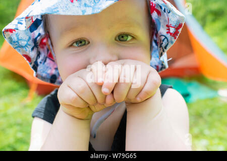 A two year old boy camping and wearing a sun hat. Stock Photo