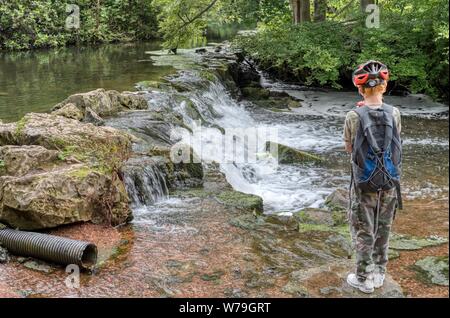 Boy watching a gentle waterfall at Clumber Park, Nottinghamshire, UK Stock Photo