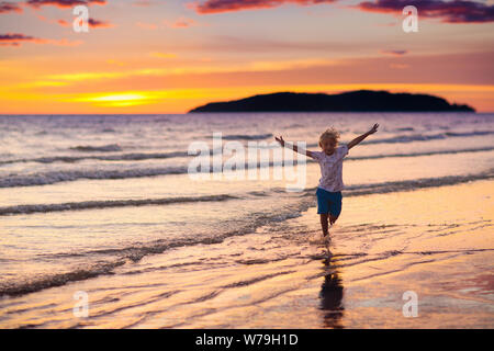 Child playing on ocean beach. Kid jumping in the waves at sunset. Sea vacation for family with kids. Little boy running on tropical beach of exotic is