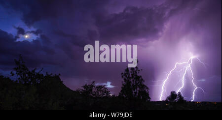 The moon is still visible as a lightning storm moves in. Stock Photo