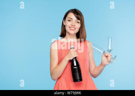 Happy gorgeous girl with toothy smile holding bottle of champagne and two flutes Stock Photo