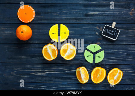 Сolorful math fractions and oranges as a sample on dark wooden background or table. Interesting creative funny math for kids. Education, back to schoo