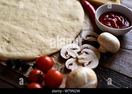 Close-up of rolled pizza dough with cherry tomatoes, mushrooms, sauce and chili Stock Photo