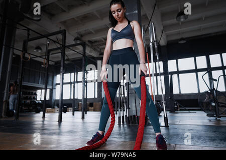 Fit woman using battle ropes during strength training at the gym. Athlete moving the ropes for burning fats at health club. Stock Photo