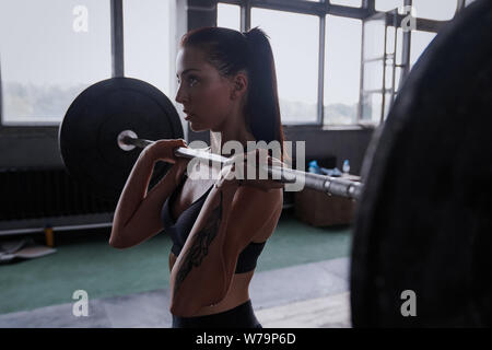 Focused on success. Attractive strong muscular female bodybuilder doing heavy duty squats lifting barbell at the crossfit gym Stock Photo