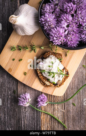 A delicious garlic and chive cream cheese spread on herbed crackers next to a bowl of purple chive flowers. Stock Photo
