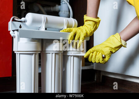 Plumber in yellow household gloves changes water filters. Repairman installing water filter cartridges in kitchen. Drinkable water filtration system Stock Photo
