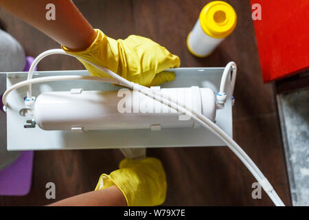 Plumber in yellow household gloves changes water filters. Repairman installing water filter cartridges in kitchen. Drinkable water filtration system i Stock Photo