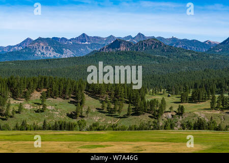 Landscape scene of a ranch with an old cabin, fields, forest, and high snow-capped mountain peaks in the Rocky Mountains near Pagosa Springs, Colorado Stock Photo