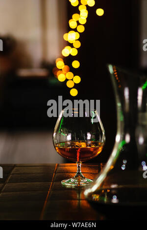 Snifter of brandy in elegant glass with space for text on dark colorful background. Decanter defocussed. Traditional French drink. Stiff drink. Servic Stock Photo