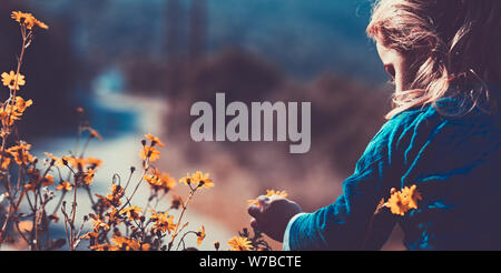 Cute little boy enjoying little gentle orange wildflowers, walking at the evening, with pleasure spending time in countryside Stock Photo