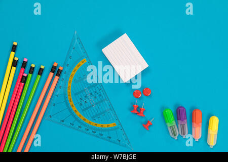 Colored crayons, transparent triangular ruler, pile of white scratch paper, a group of red pushpins, four colorful highlighters are scattered on a Stock Photo