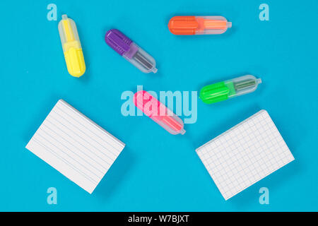 Five multicolored text markers and two piles of white scratch papers on azure background cutout Stock Photo