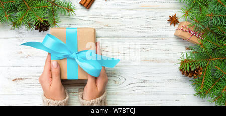female hands hold wrapping christmas gift box with blue ribbon on white wooden table. banner Top view. Stock Photo