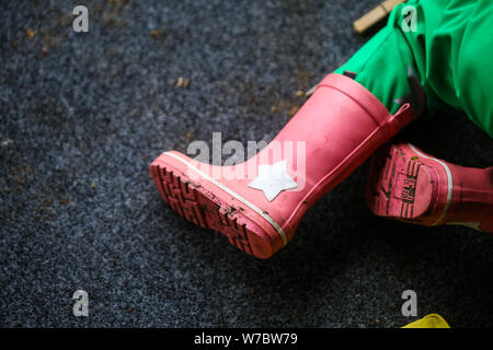 Details with the pink rubber boots and green jumpsuit of a little girl during a rainy day Stock Photo