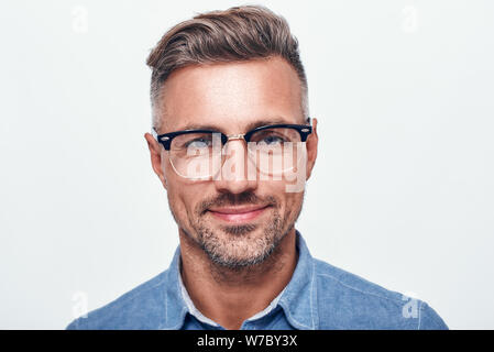 Happy and handsome. Close up portrait of charming bearded man in eyewear looking at camera and smiling while standing against grey background. Men beauty. Studio shot Stock Photo