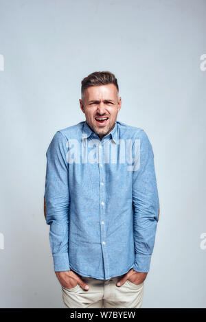 I don't like it. Frustrated young man keeping hands in his pockets and making unhappy face while standing against grey background. Stress concept Stock Photo
