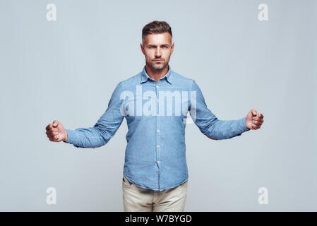 I am strong. Confident and handsome bearded man in casual clothes keeping hands clenched in fists while standing against grey background. Strength and motivation. Studio shot Stock Photo