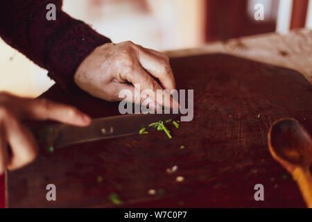 Shallow depth of field image with details of an old lady hands chopping parsley on a wooden cutting board Stock Photo