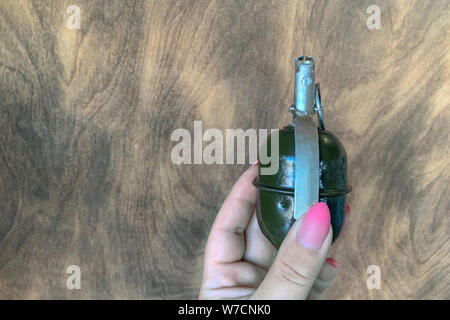 hand grenade in girl hand on wooden background. copy space Stock Photo