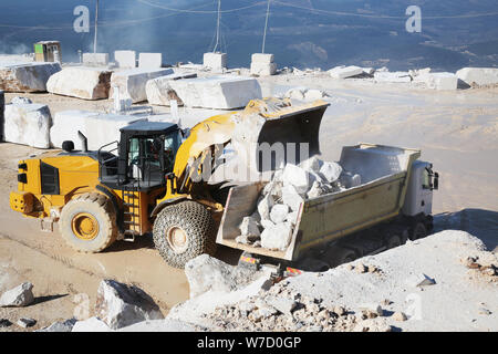 A loader working in marble quarry. Loader carrying marble block. Heavy equipment loader working site. Wheel loader working marble mine. Stock Photo