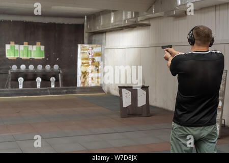 Man in shooting range in shooting action with GLOCK 19, view from behind o holding a pistol taking aim away from the camera with shallow depth of fiel Stock Photo