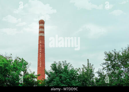 Smokestack in shape of wine bottle neck with text In vino veritas. Industrial chimney on cloud sky background and tree crowns. Manufacturing of alcoho Stock Photo