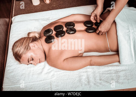 Masseuse setting up stones on the back of her client. Stock Photo
